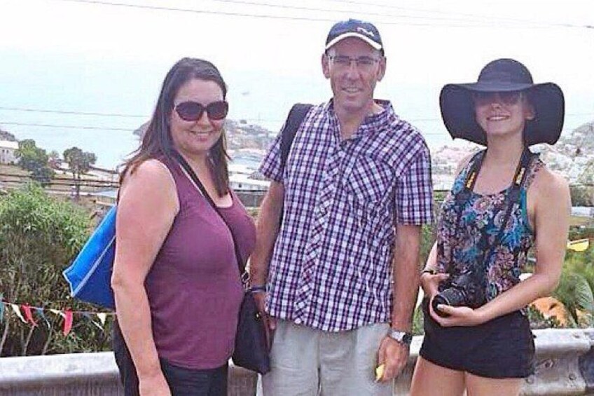 Three people standing on a bridge with a scenic view of a coastal landscape. 4