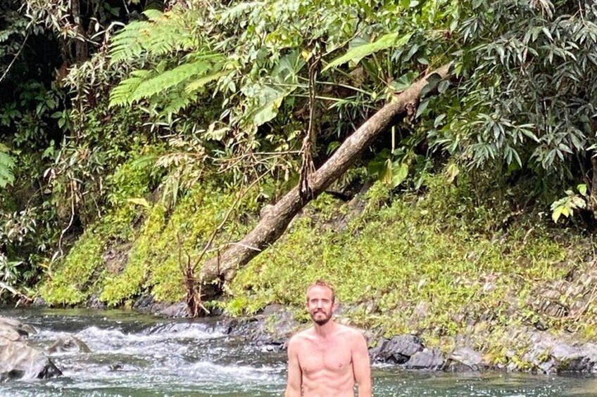 A man standing in a flowing river surrounded by dense greenery and a fallen tree. 4