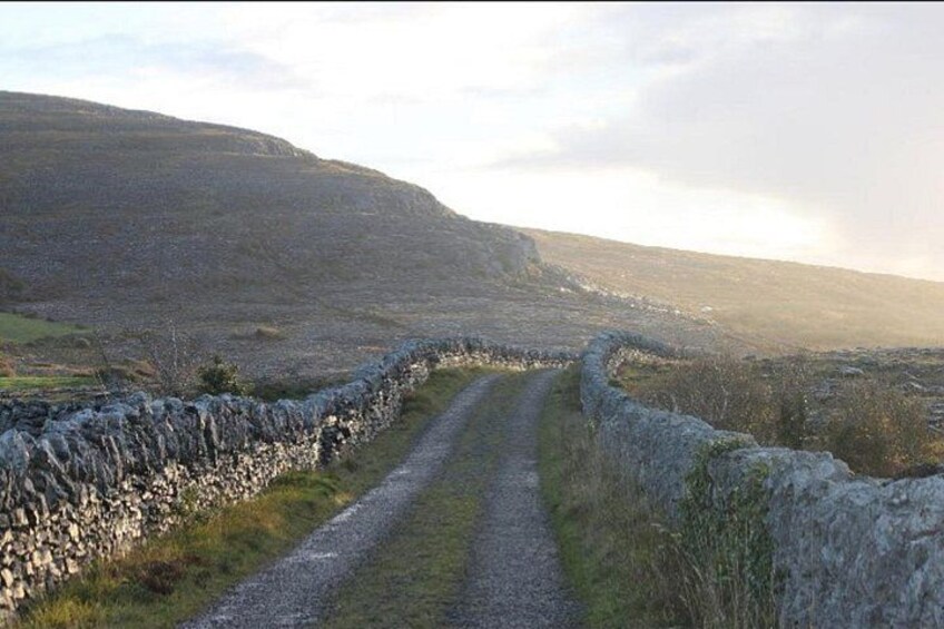 A rural road bordered by stone walls, leading through a hilly landscape. 2