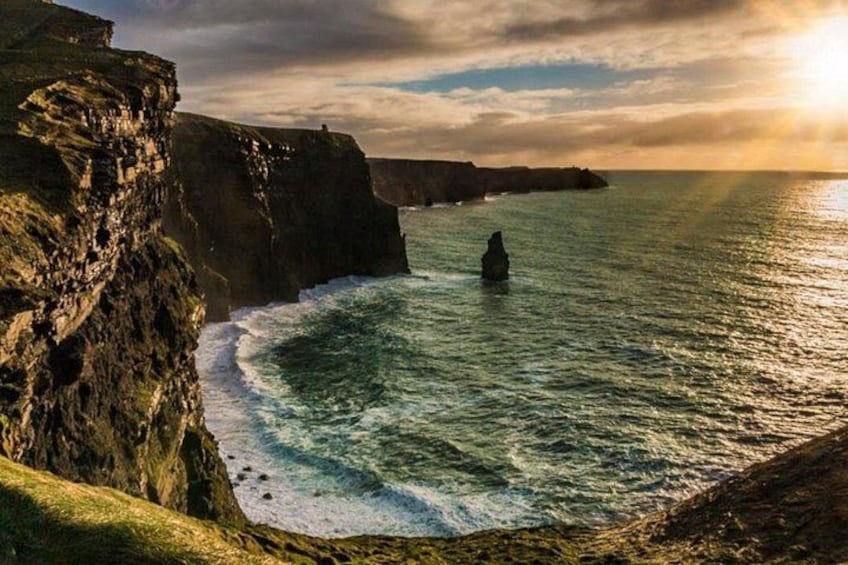 A rocky coastline with waves crashing against the cliffs and a person standing in the water. 1