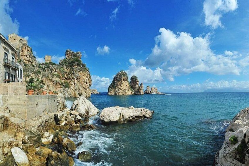 Un paisaje costero con acantilados rocosos, mar azul cristalino y un edificio a la izquierda. 2