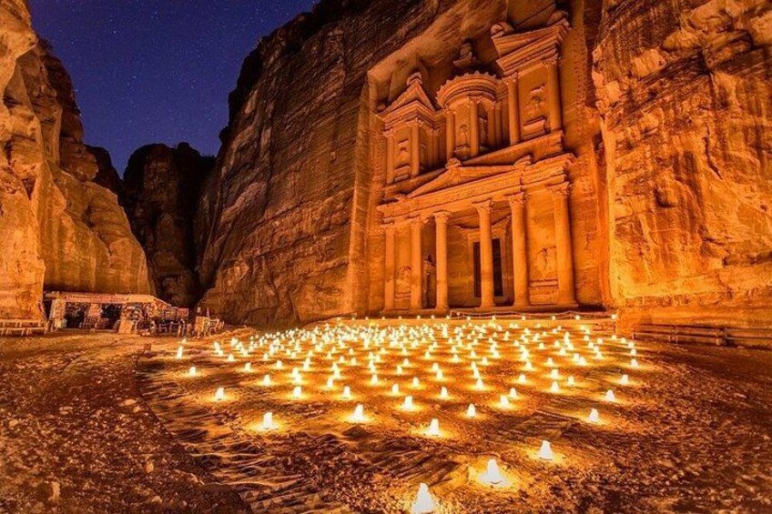 Una struttura scavata nella roccia, caratterizzata da una serie di colonne e un'ampia facciata, illuminata da numerose candele sul terreno. 3