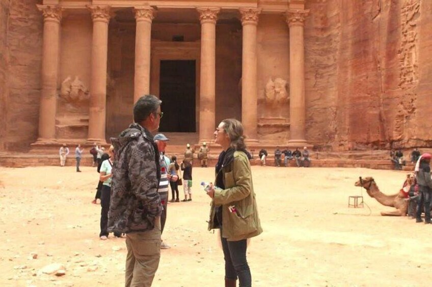 Un'imponente struttura antica in pietra con colonne, un cammello e persone in un paesaggio desertico. 2