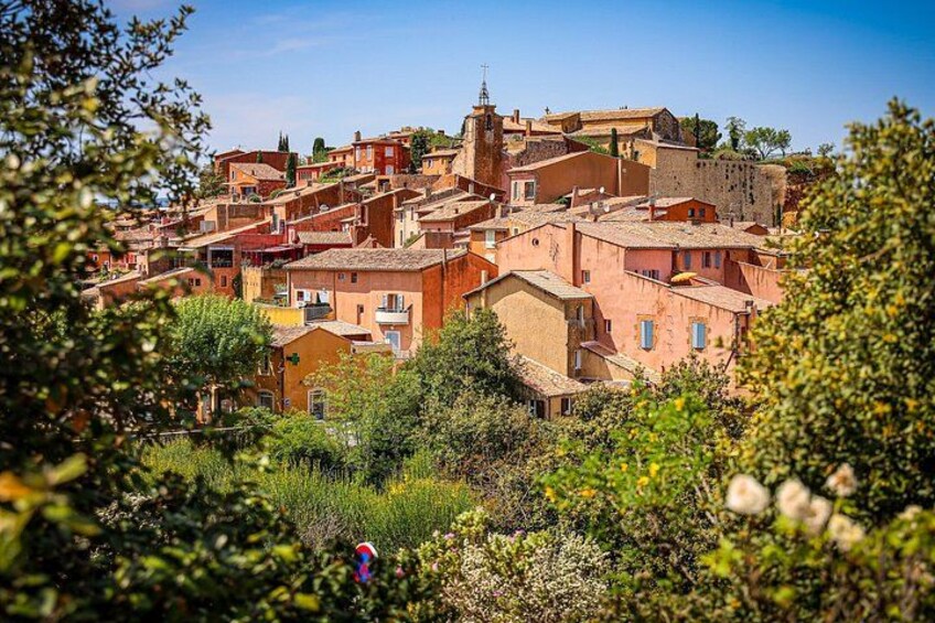 A hillside town with terracotta-roofed buildings, lush greenery, and a clear blue sky. 1