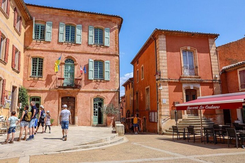 A red building with green shutters, a café with outdoor seating, and a group of people standing on the sidewalk. 2