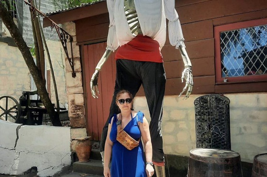 Eine Person steht vor einer Skeletfigur, im Hintergrund ein Gebäude und ein Baum. 5
