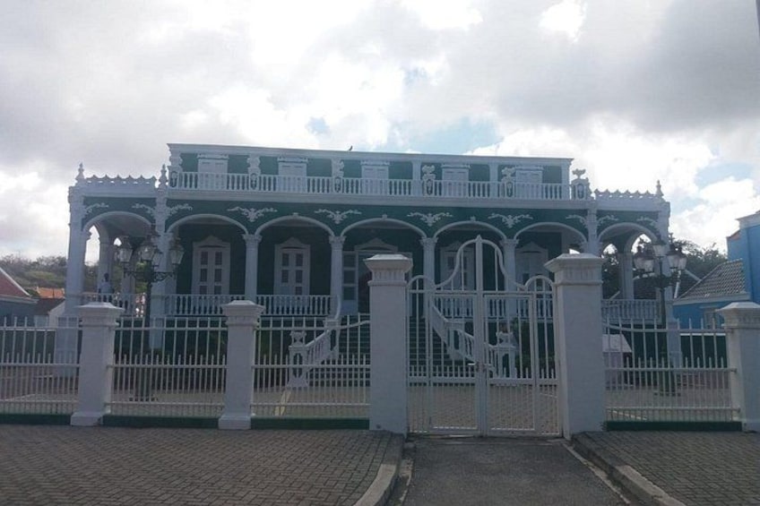 A large, ornate building with a green facade and white trim, surrounded by a white fence. 2