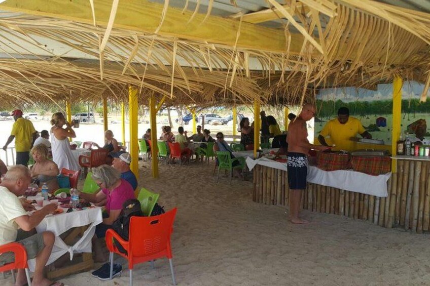 A beachside restaurant with patrons dining under a thatched roof. 2