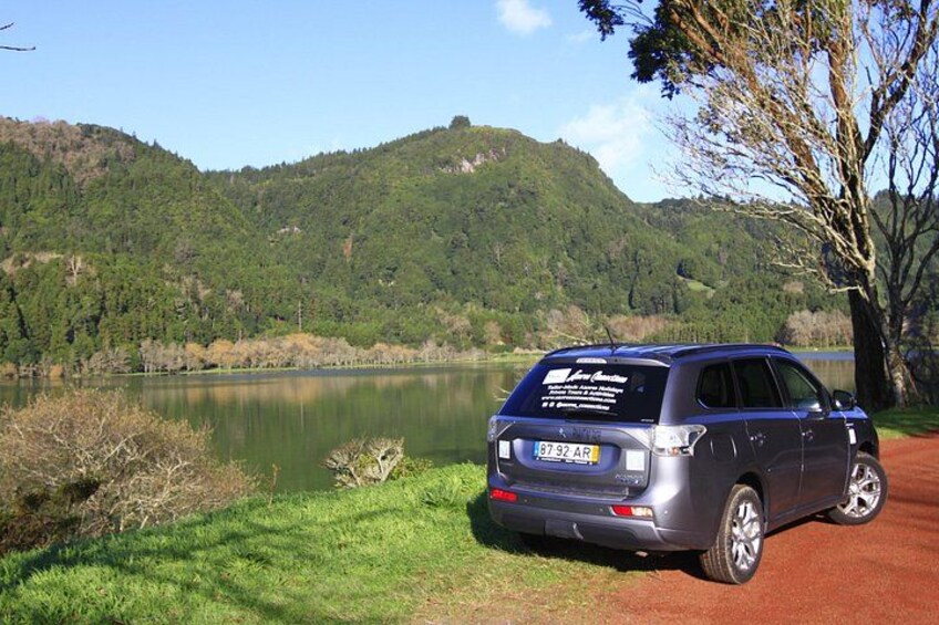 A car parked by a lake with a forested hill in the background. 1