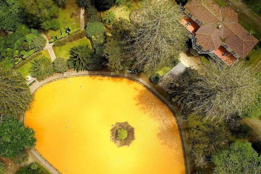 An aerial view of a large yellow pond surrounded by trees and a building with a red roof. 4