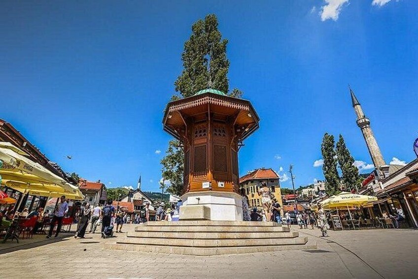 A central square with a traditional wooden pavilion, a mosque with a minaret, and surrounding shops. 1