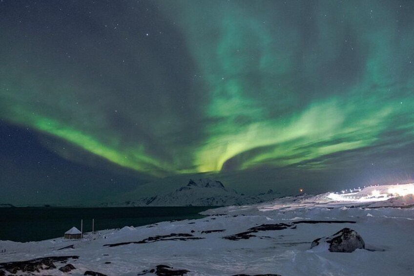 Nordlys over et snøklædt landskab med et bjerg i baggrunden. 2