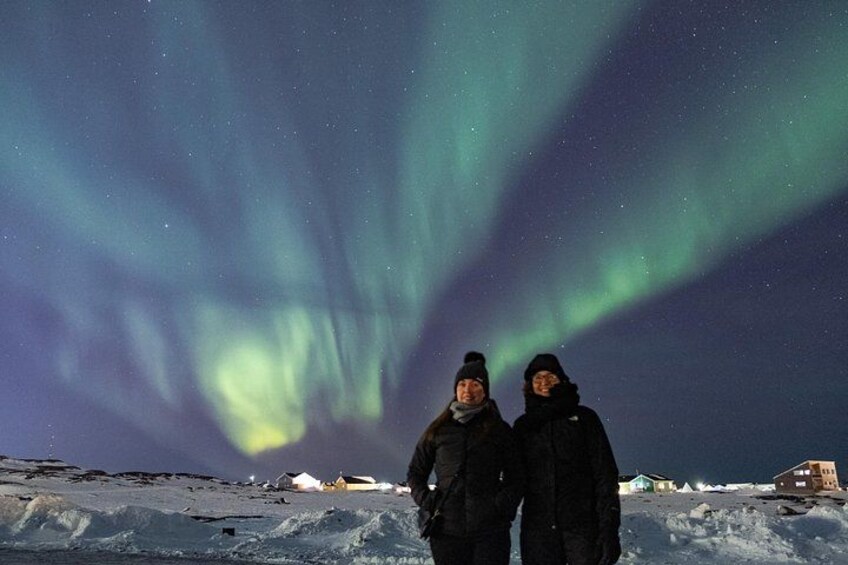 Deux personnes se tiennent debout dans un paysage enneigé, avec des aurores boréales en arrière-plan. 3