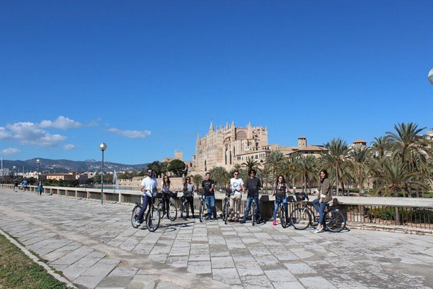 Un groupe de personnes à vélo circule sur une promenade pavée, avec un bâtiment historique en arrière-plan. 4