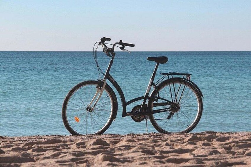 A bicycle parked on a sandy beach with the ocean in the background. 2