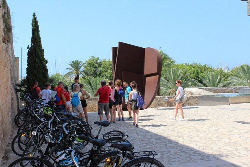 A group of people standing near bicycles and a large brown sculpture in an outdoor setting. 4