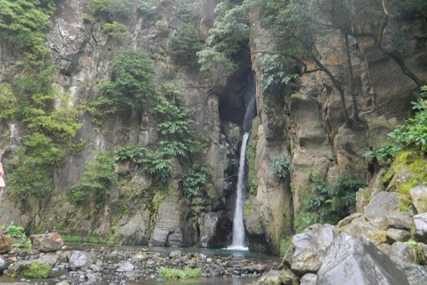 A waterfall cascading down a rocky cliff surrounded by lush greenery. 1