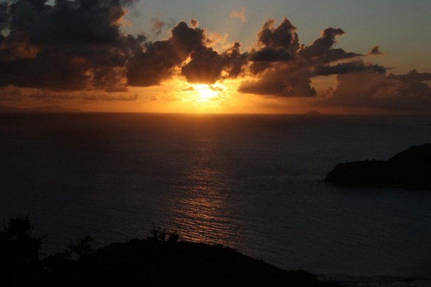 A sunset over the ocean with clouds and a silhouette of land. 1
