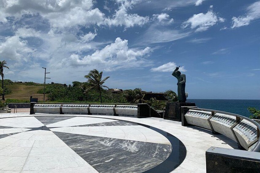 En rund plads med en statue, palmer og udsigt til havet. 3