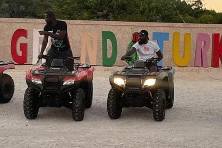 Two people on ATVs in front of a colorful sign. 5