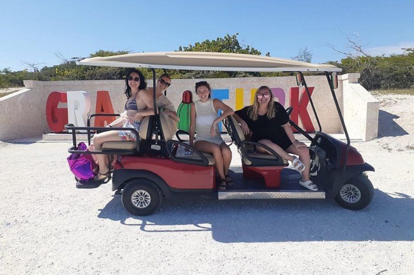 A golf cart with four people, a sign with large letters, and a clear sky. 1