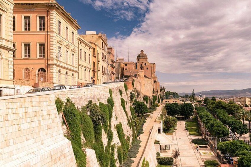 A historic cityscape with a prominent fortress, a stone wall with greenery, and a clear sky. 4