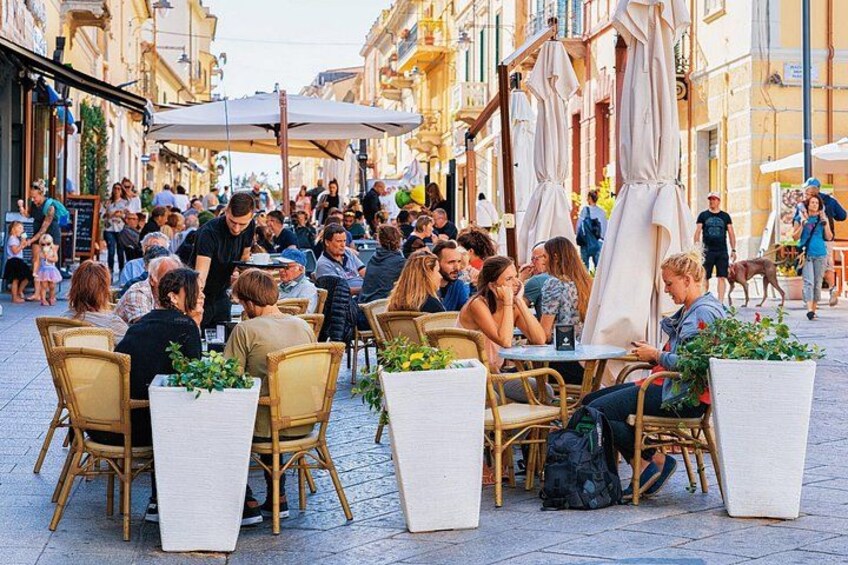 A bustling outdoor café with wicker chairs and tables, surrounded by pedestrians and buildings. 3