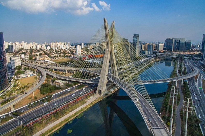 A cable-stayed bridge with multiple lanes of traffic, a river below, and a cityscape in the background. 1