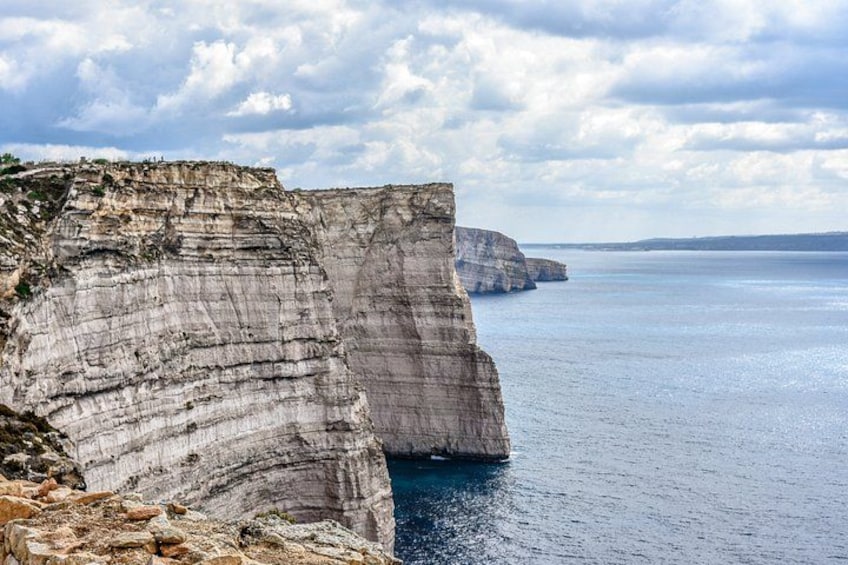 A coastal cliff with layered rock formations and a calm sea. 2