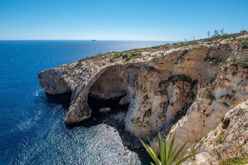 A coastal cliff with a natural arch formation and a clear blue sea. 1
