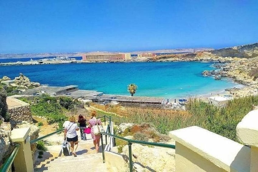 A coastal landscape with a clear blue sea, a rocky shoreline, and a staircase leading down to the beach. 3