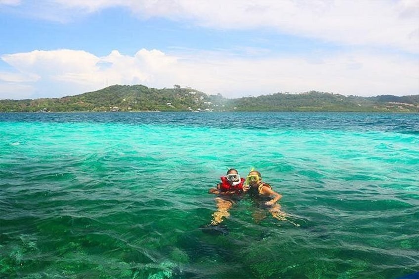 Dos personas haciendo snorkel en aguas turquesas cristalinas con un paisaje montañoso al fondo. 2