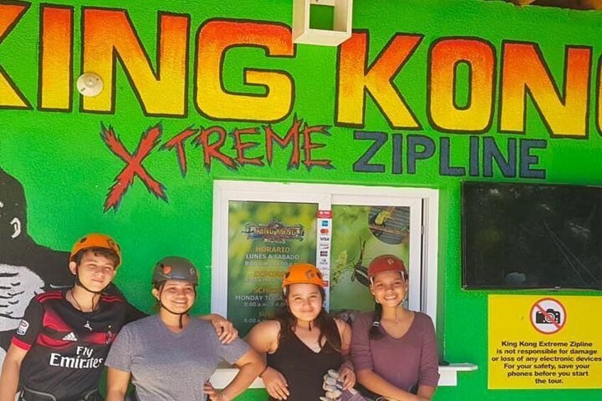 A green wall with the text 'KING KONG Xtreme ZIPLINE' and a group of people wearing hats. 1