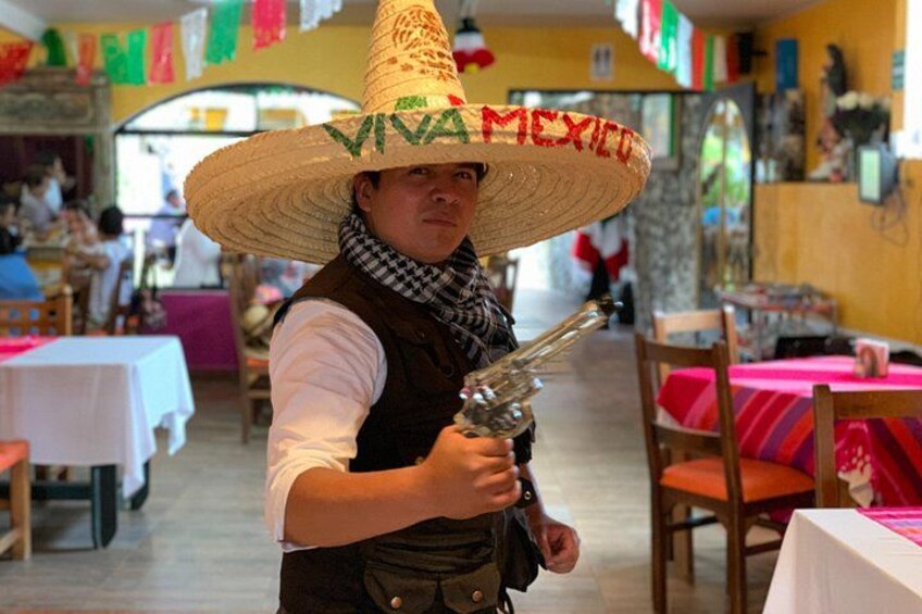 Eine Person mit Sombrero und traditioneller Kleidung hält in einem Restaurant eine Spielzeugpistole. 4