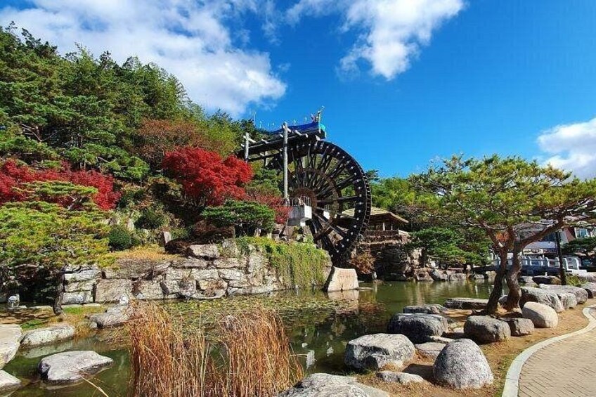 A traditional water wheel, a pond, rocks, and red foliage in a landscaped garden. 1