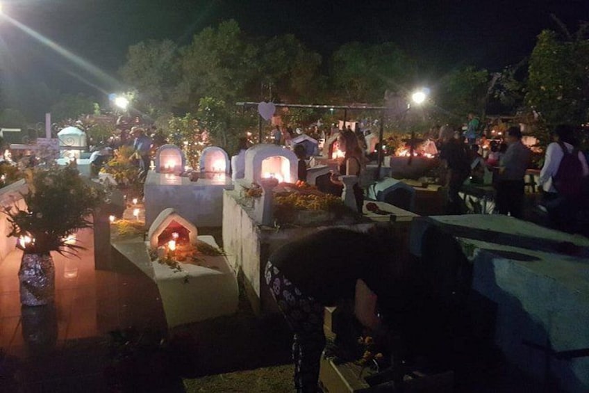 Reunión nocturna al aire libre con tumbas iluminadas y gente alrededor. 1