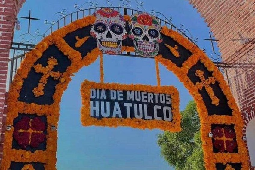 Un arco decorado con calaveras y flores, con un letrero que dice 'DIA DE MUERTOS HUATULCO'. 3