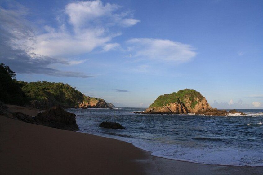 Una playa con una isla rocosa, cielo despejado y mar tranquilo. 2