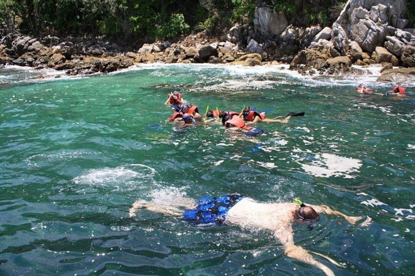 Personas haciendo snorkel en aguas cristalinas con costas rocosas. 5