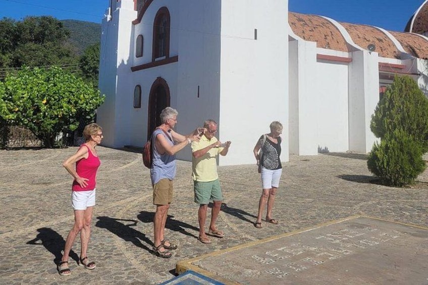 A group of people standing in front of a white building with a red roof, possibly a church, on a sunny day. 4