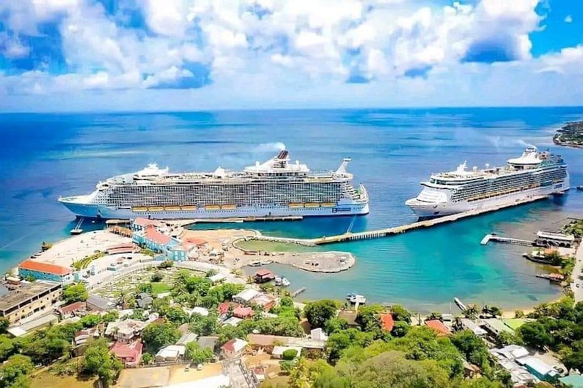 A cruise ship port with two large cruise ships docked, surrounded by a small town and clear blue waters. 1