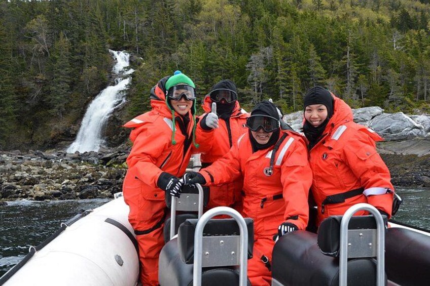 A group of people in orange jackets on a white inflatable boat near a waterfall. 3
