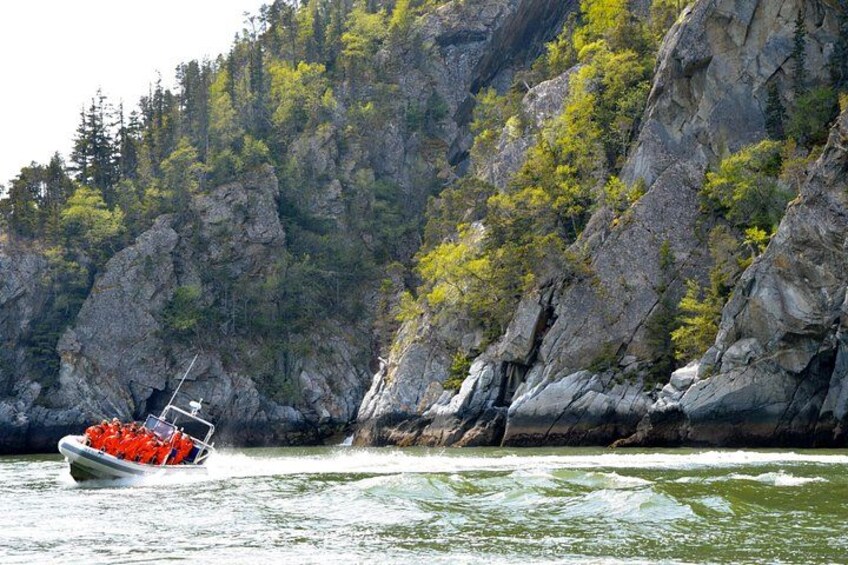A boat with red life jackets on a river surrounded by rocky cliffs and trees. 2