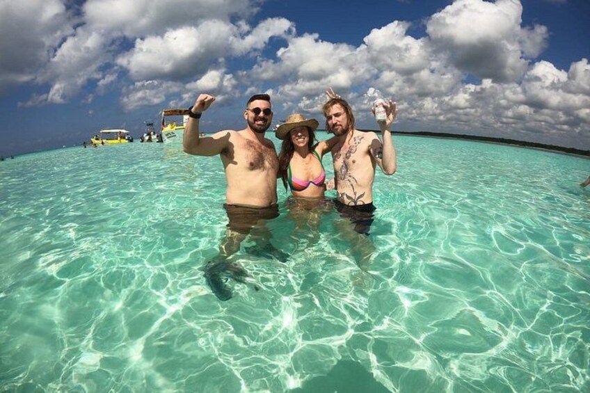 Tres personas en agua turquesa cristalina, con un bote y un cielo parcialmente nublado al fondo. 3