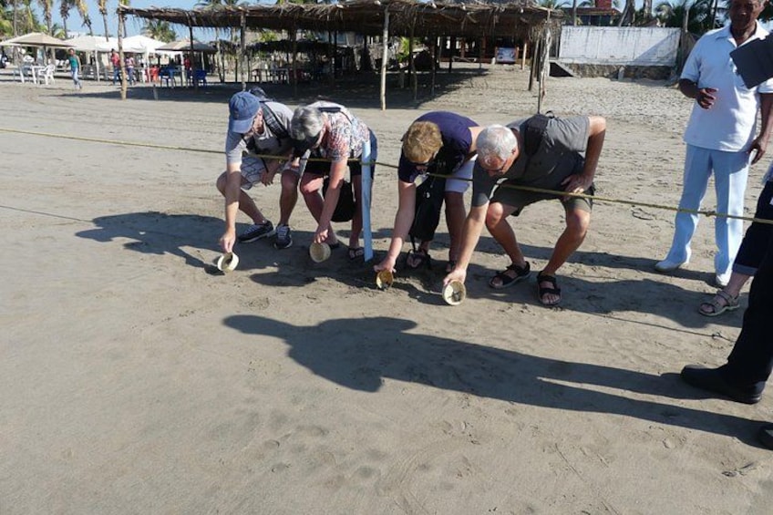 Des personnes se trouvent sur une plage de sable, certaines sont penchées, peut-être en train de jouer à un jeu ou de creuser. 4