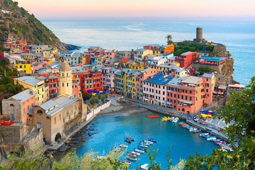 Une ville côtière aux bâtiments aux couleurs vives, un port où sont amarrés des bateaux et un château perché sur une colline. 1