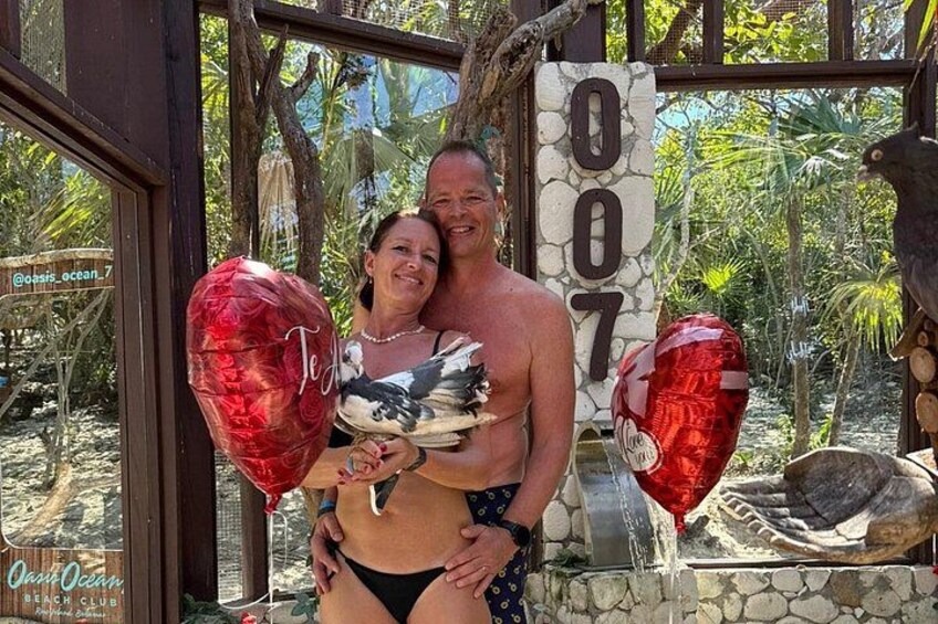 Un couple pose devant une structure ornée d’un symbole « # », entourée d’une végétation tropicale. 2