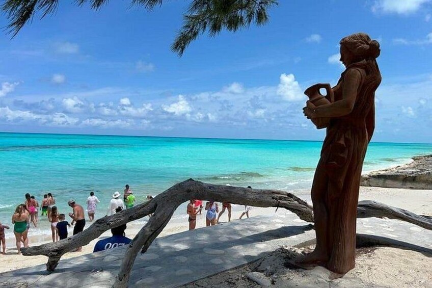 Une plage avec une sculpture représentant une femme tenant une tasse, des personnes en arrière-plan et une eau turquoise. 5