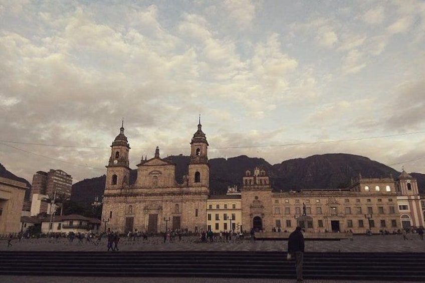 A historic building with two towers, a large plaza, and mountains in the background. 3