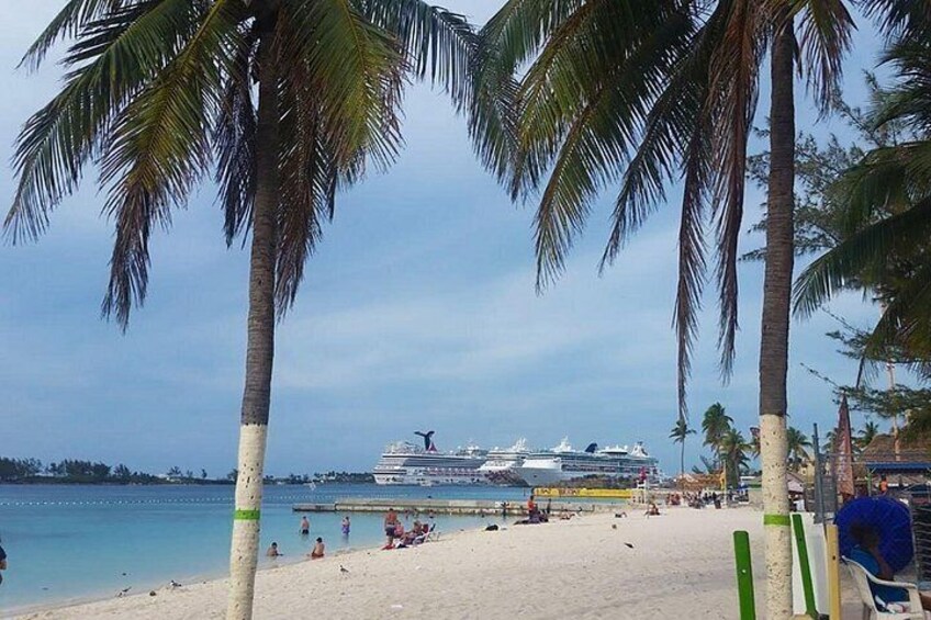 A beach with palm trees, a cruise ship, and people on the sand. 2